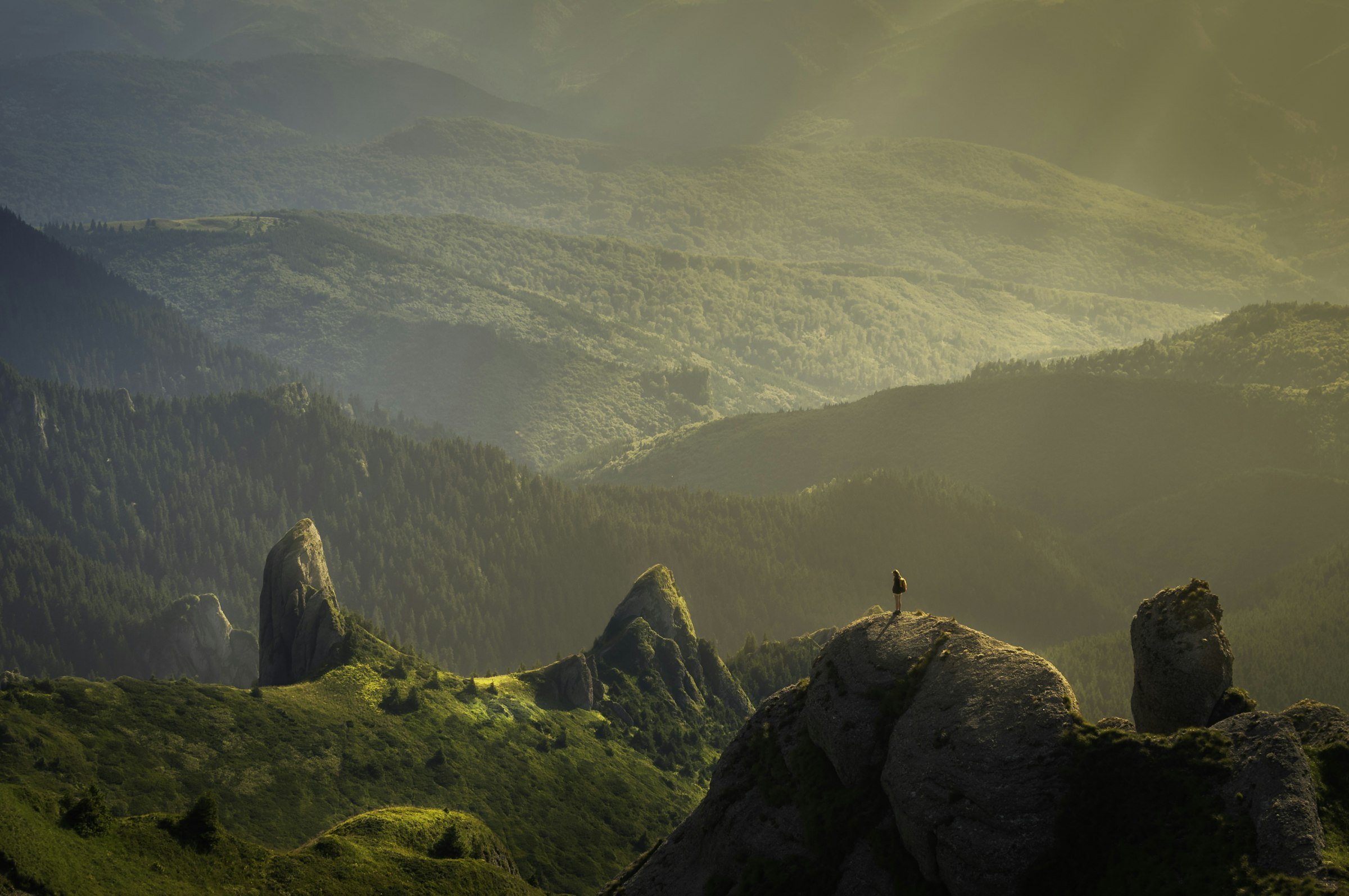 Sunlit green mountain ridges at golden hour with a small figure standing on a distant peak